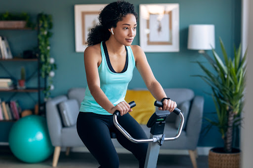Shot of sporty young woman exercising on smart stationary bike and listening to music at home.